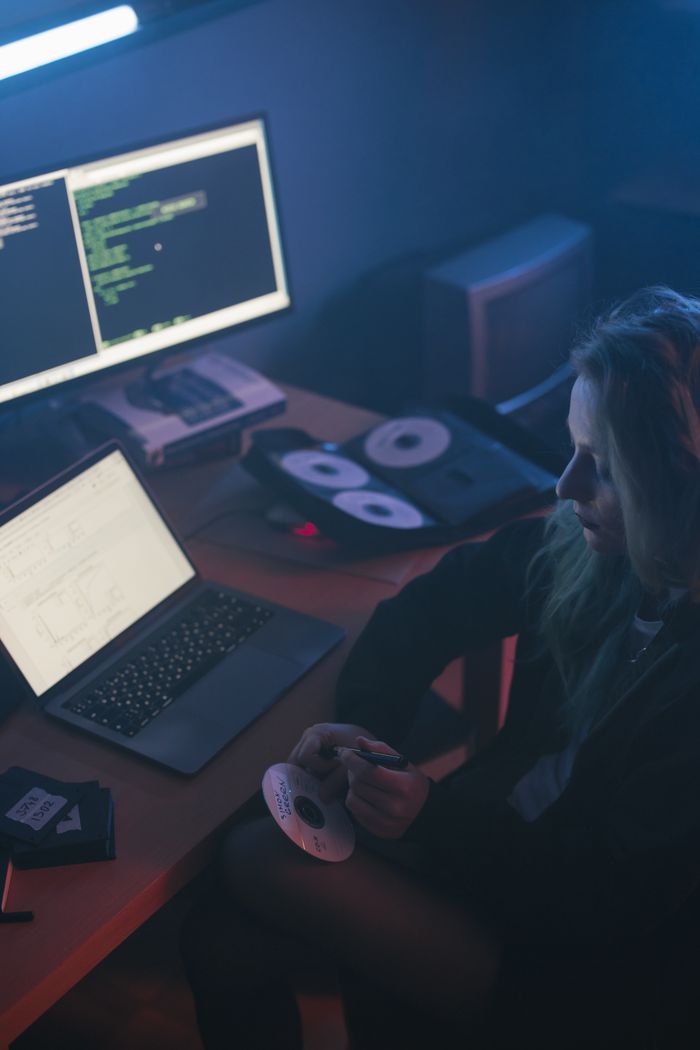 portfolio-05 Woman working on a laptop with code on screen, sitting in a dimly lit office holding a CD.