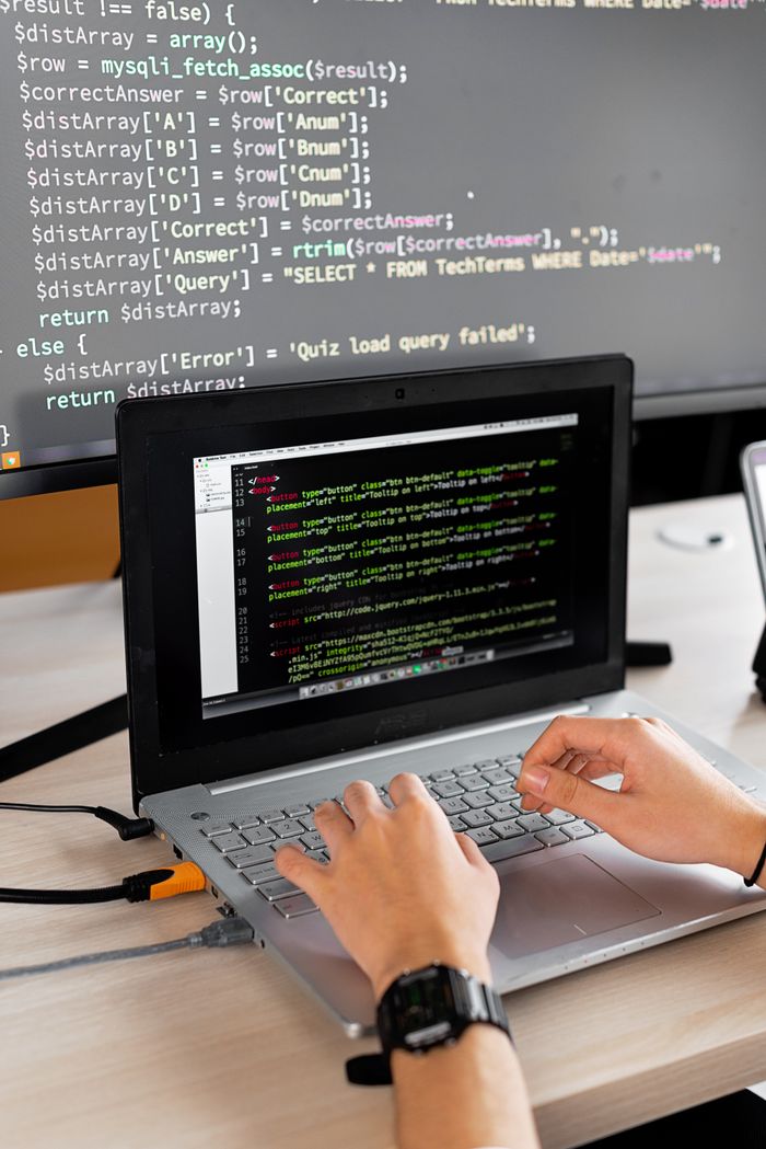 portfolio-02 Person coding at a desk with laptop and external monitor showing programming code.